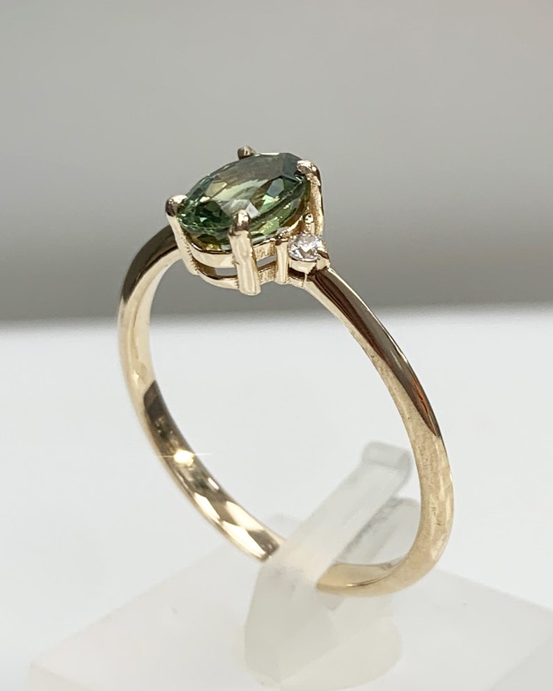 May include: A gold ring featuring a green oval gemstone and a smaller diamond accent.
