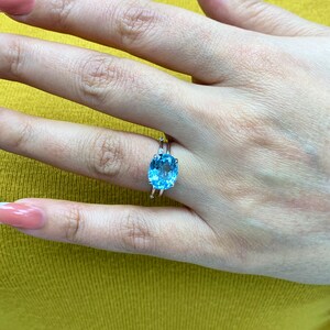 May include: A silver ring with a large oval-shaped blue topaz gemstone. The ring is set with smaller diamonds on the band.