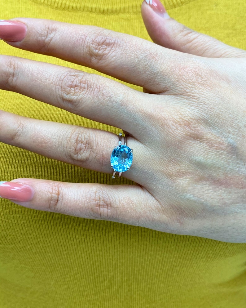 May include: A silver ring with a large oval-shaped blue topaz gemstone. The ring is set with smaller diamonds on the band.