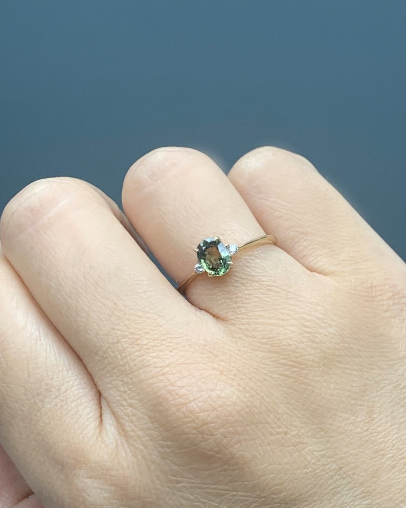 May include: A gold ring featuring a green oval gemstone and two smaller white gemstones set into the band.