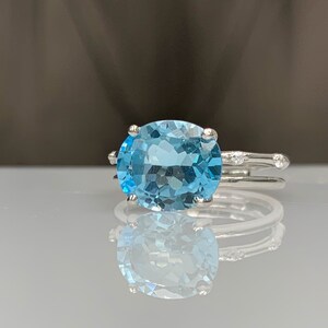 May include: A silver ring with a large oval-shaped blue topaz gemstone. The ring has a delicate band with small diamonds on the sides.