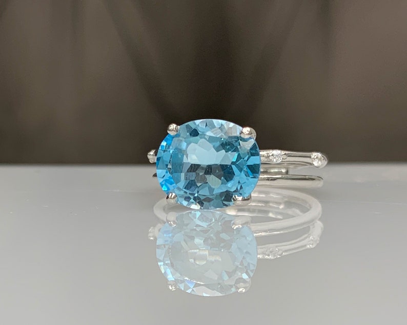 May include: A silver ring with a large oval-shaped blue topaz gemstone. The ring has a delicate band with small diamonds on the sides.