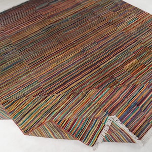 May include: A rectangular area rug featuring a dense pattern of thin, multicolored horizontal stripes in shades of red, blue, yellow, green, and orange. The rug has a woven texture and includes short white fringe detailing along the edges.