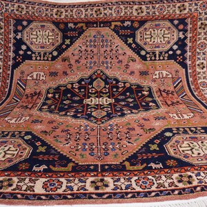 May include: A rectangular, hand-knotted rug with a central medallion design. The rug features a salmon-colored field with navy blue and rust-colored borders and accents. Intricate floral and geometric patterns adorn the rug's surface, with a fringe along the edges.