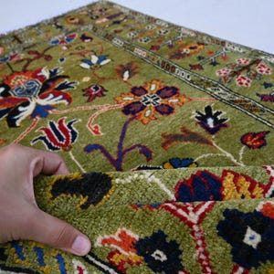 May include: A green rug with a floral pattern in shades of red, blue, yellow, and white. The rug has a border with a geometric pattern.