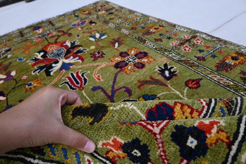 May include: A green rug with a floral pattern in shades of red, blue, yellow, and white. The rug has a border with a geometric pattern.