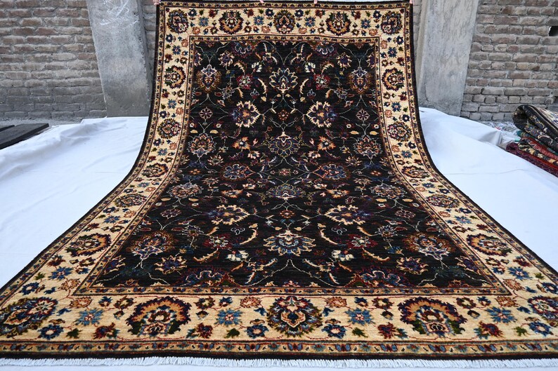 May include: A traditional Persian rug with a dark blue background and intricate floral patterns in shades of red, cream, and brown. The rug has a cream-coloured border with floral motifs.