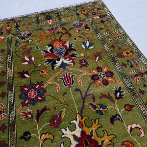 May include: A green rug with a floral pattern in shades of red, yellow, and blue. The rug has a border with a geometric design.