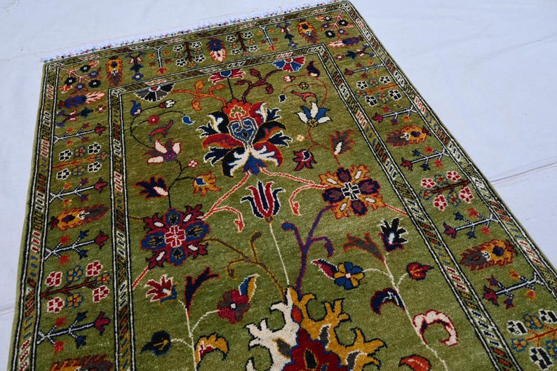 May include: A green rug with a floral pattern in shades of red, yellow, and blue. The rug has a border with a geometric design.