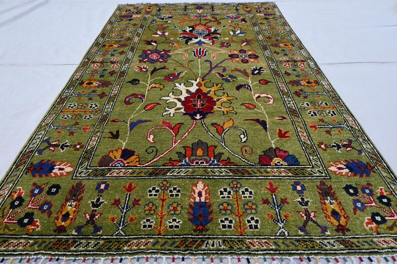 May include: A green rug with a floral pattern in shades of red, yellow, blue, and black. The rug has a border with a geometric design.