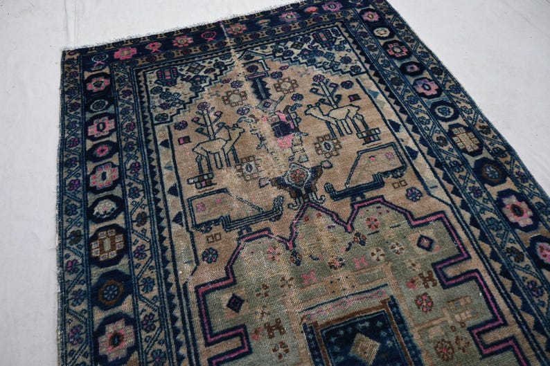 Peut inclure: Tapis ancien avec un champ central beige orn&eacute; de motifs stylis&eacute;s d'animaux et de fleurs roses et bleus. Le tapis a une bordure bleu fonc&eacute; avec des motifs floraux et des formes g&eacute;om&eacute;triques r&eacute;p&eacute;titifs. Le design du tapis est sym&eacute;trique et pr&eacute;sente des signes d'usure.