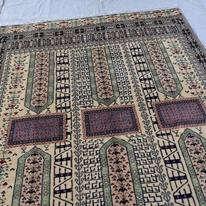 Pu&ograve; includere: Un tappeto beige con motivi intricati in tonalit&agrave; di blu, verde e rosso. Il tappeto presenta un design tradizionale con forme geometriche ripetute e motivi floreali.
