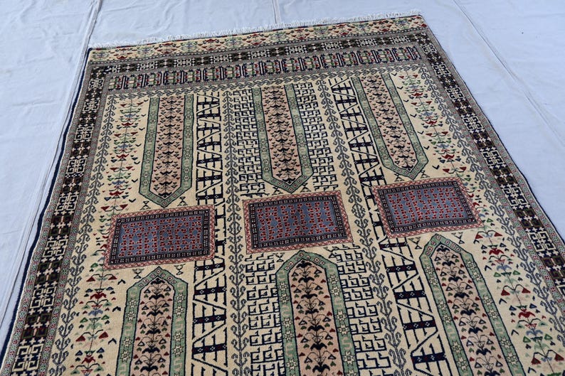 Pu&ograve; includere: Un tappeto beige con motivi intricati in tonalit&agrave; di blu, verde e rosso. Il tappeto presenta un design tradizionale con forme geometriche ripetute e motivi floreali.
