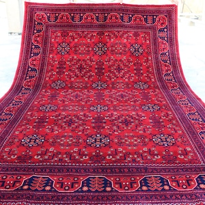 May include: A red rug with a blue and white patterned border. The rug has a traditional Persian design with intricate floral motifs.