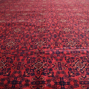 May include: A red rug with a geometric pattern in shades of blue and cream. The rug has a traditional Persian design.