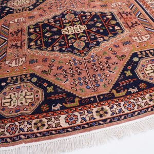 May include: An antique rug with a central medallion design in shades of coral, navy, and cream. The rug features intricate floral and geometric patterns, with a fringed edge. The overall design is symmetrical and detailed.