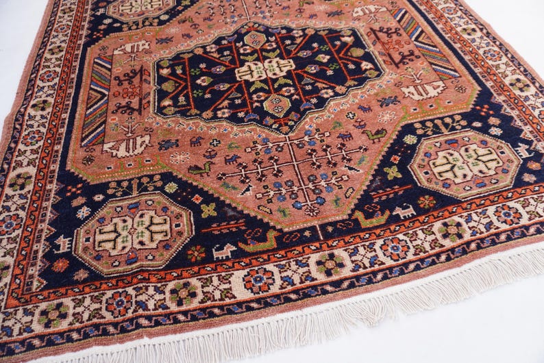 May include: An antique rug with a central medallion design in shades of coral, navy, and cream. The rug features intricate floral and geometric patterns, with a fringed edge. The overall design is symmetrical and detailed.