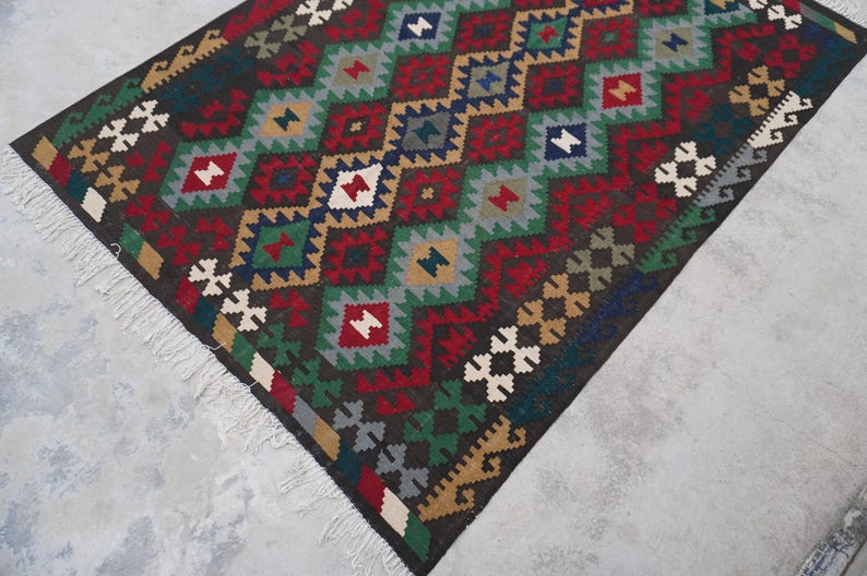 May include: A colorful rug with a geometric pattern in shades of red, green, blue, brown, and white. The rug has a fringe border.