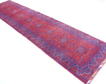 Op de afbeelding: Een lang, smal rood en blauw tapijt met een geometrisch patroon. Het tapijt heeft franjes aan de uiteinden.