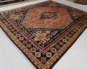 May include: A rectangular area rug featuring a large central medallion in shades of coral and black. The border displays intricate geometric and floral motifs in colors including blue, green, yellow, and cream, finished with a white fringe edge.