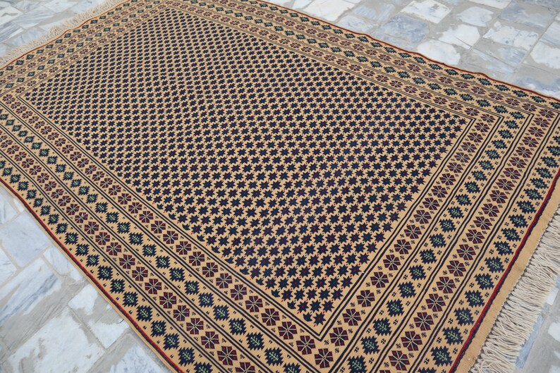 May include: A beige rug with a black and blue geometric pattern. The rug has a red and green border with a fringe.