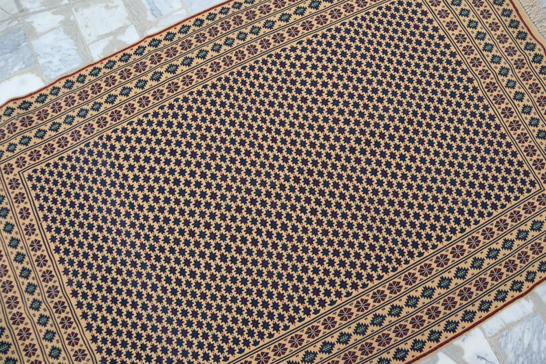 May include: A beige rug with a black and white geometric pattern. The rug has a border with a floral design in shades of red, green, and blue.