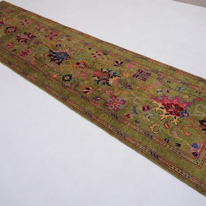 May include: A green runner rug with a floral pattern in shades of pink, red, blue, and yellow. The rug has a fringed edge.