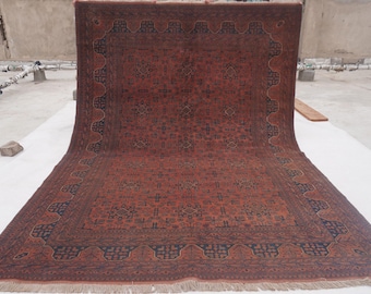 May include: A large, rectangular rug with a detailed, geometric pattern in shades of red and dark blue. The rug has a fringed edge and a central medallion design. The overall aesthetic is traditional and ornate, suitable for home decor.