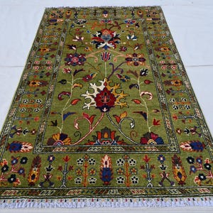May include: A green rug with a floral pattern in shades of red, yellow, and blue. The rug has a border with a geometric pattern.