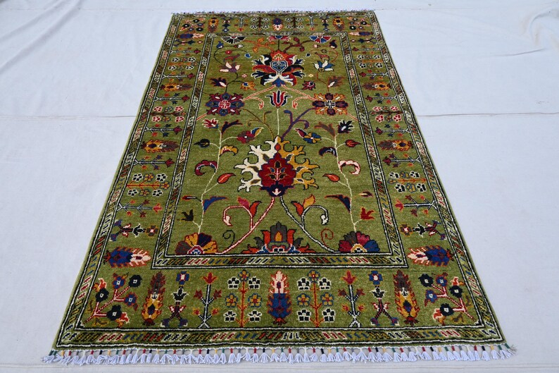 May include: A green rug with a floral pattern in shades of red, yellow, and blue. The rug has a border with a geometric pattern.
