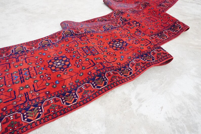 May include: A red runner rug with a traditional Persian design featuring intricate blue and green patterns. The rug is folded in half, showcasing the detailed craftsmanship.