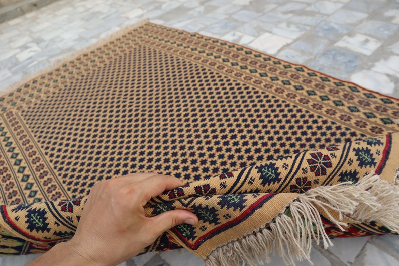 May include: A beige rug with a geometric pattern in shades of blue, red, and green. The rug has a fringe border and is folded in half.