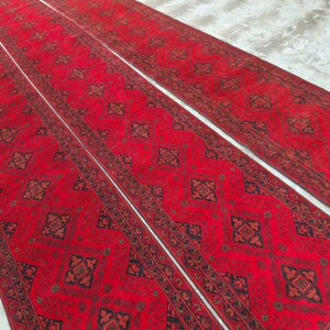 K&ouml;nnte beinhalten: Drei rote L&auml;ufer mit aufwendigen geometrischen Mustern in Schwarz und Braun. Die Teppiche sind nebeneinander angeordnet und zeigen ihre L&auml;nge und ihr Design. Der Hintergrund ist eine hellfarbige Oberfl&auml;che.