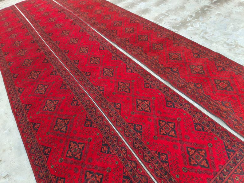 K&ouml;nnte beinhalten: Drei rote L&auml;ufer mit aufwendigen geometrischen Mustern in Schwarz und Braun. Die Teppiche sind nebeneinander angeordnet und zeigen ihre L&auml;nge und ihr Design. Der Hintergrund ist eine hellfarbige Oberfl&auml;che.