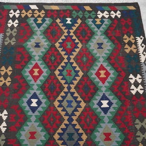 May include: A traditional rug with a geometric pattern in shades of red, blue, green, and brown. The rug has a diamond-shaped design with intricate details.