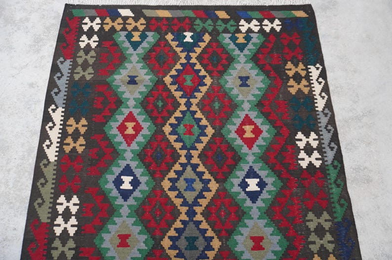 May include: A traditional rug with a geometric pattern in shades of red, blue, green, and brown. The rug has a diamond-shaped design with intricate details.