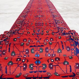 May include: A red, blue, and green patterned rug is rolled up and stacked. The rug has a traditional design with intricate details.