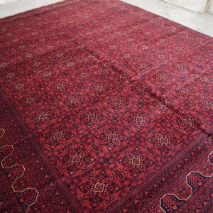 May include: A red rug with a detailed geometric pattern in shades of blue and cream. The rug has a fringed edge.