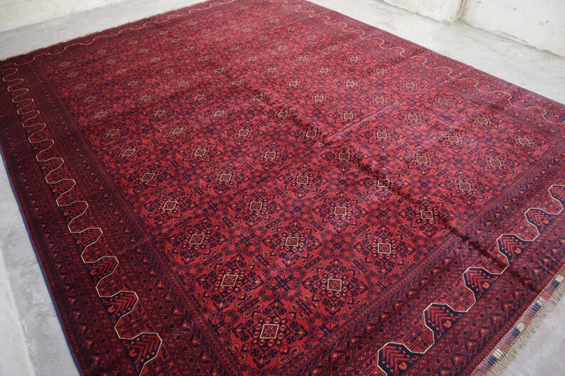 May include: A red rug with a detailed geometric pattern in shades of blue and cream. The rug has a fringed edge.