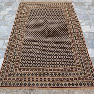 May include: A beige rug with a black and white geometric pattern and a red, green, and blue border. The rug has fringe on the edges.