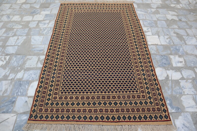 May include: A beige rug with a black and white geometric pattern and a red, green, and blue border. The rug has fringe on the edges.