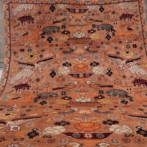May include: A rectangular area rug featuring a warm orange background with a repeating pattern of birds, deer, and floral motifs in shades of white, black, and dark red. The design includes symmetrical arrangements of avian figures and stylized animals.