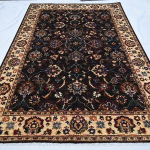 May include: A dark brown rug with a cream-coloured border. The rug has a floral pattern with intricate details.