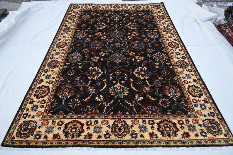 May include: A dark brown rug with a cream-coloured border. The rug has a floral pattern with intricate details.