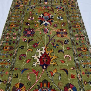 May include: A green rug with a floral pattern. The rug has a border with a repeating design. The flowers are red, yellow, and blue.