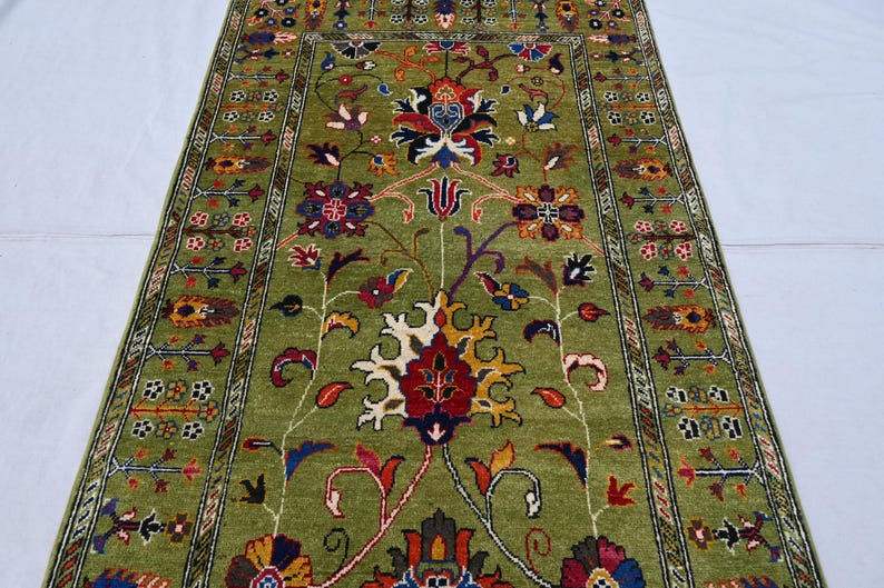 May include: A green rug with a floral pattern. The rug has a border with a repeating design. The flowers are red, yellow, and blue.