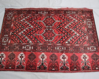 May include: A red, black, and white rug with a geometric pattern. The rug has a fringe border.
