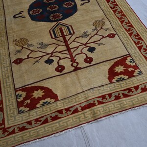 May include: A beige rug with a red, blue, and green border. The center of the rug features a stylized tree with red and blue fruit, and a blue and red circle with stars.