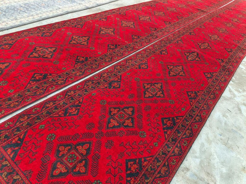 K&ouml;nnte beinhalten: Zwei rote L&auml;ufer mit aufwendigen geometrischen Mustern in Schwarz und Braun. Die Teppiche haben ein zentrales Design mit sich wiederholenden Motiven und einen detaillierten Rand. Die Teppiche sind nebeneinander platziert.