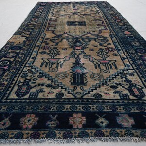 Peut inclure: Tapis ancien avec un champ central beige et une bordure bleu marine. Le tapis pr&eacute;sente des motifs complexes, notamment des motifs floraux et g&eacute;om&eacute;triques, avec des accents de rose et de bleu. Le tapis est de forme rectangulaire et a une bordure frang&eacute;e.